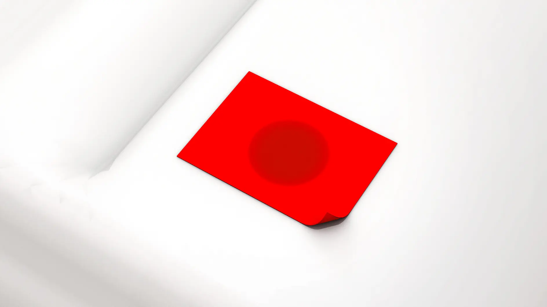 A red rectangular piece of paper or card with a subtle dark circle in the center lies on a white, textured surface. The cards corner is slightly bent upwards, secured by tesa tape.