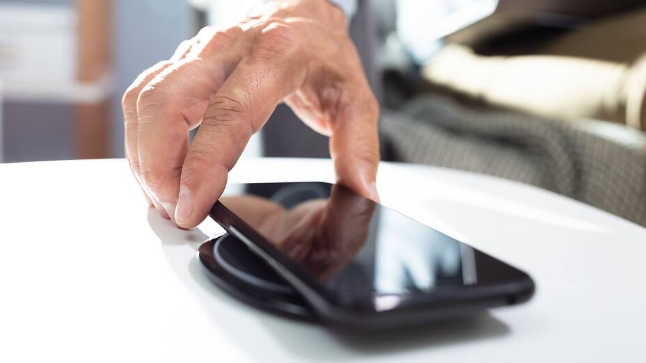 Man Charging Smartphone Using Wireless Charging Pad At Home Man Charging Smartphone Using Wireless Charging Pad At Home
