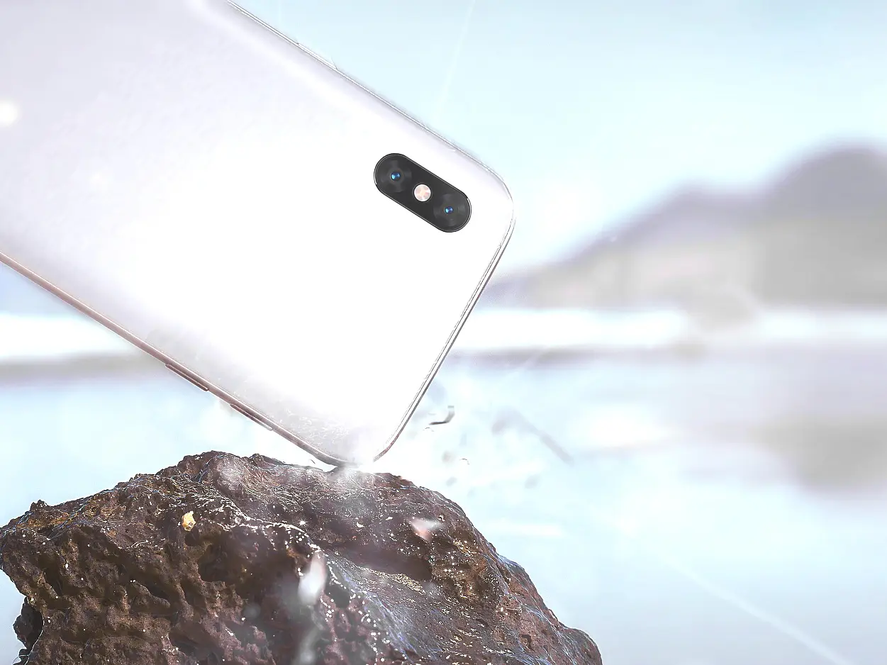 A smartphone is captured mid-air, splashing water as it drops towards a rocky surface. The background features a blurred landscape with mountains and a body of water. (This text has been generated by AI)