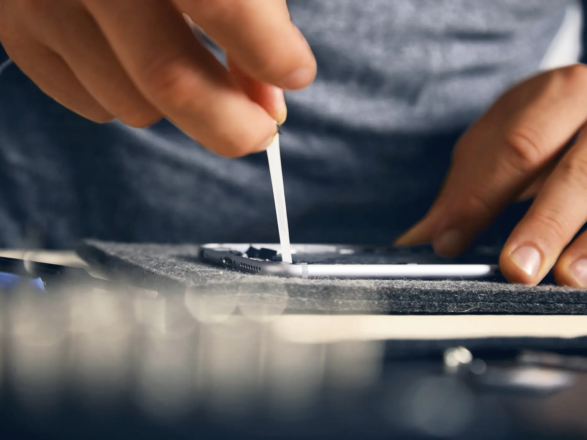 A person cleans a smartphone screen with a cotton swab, focusing on a small detail. The setting is a close-up shot that highlights the hands precision and the phones surface. Other out-of-focus objects are visible in the foreground and background. (This text has been generated by AI)