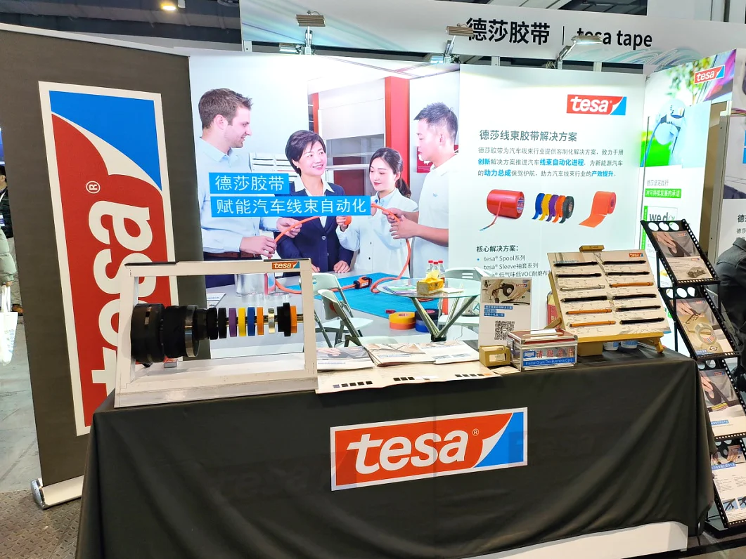 A trade show booth features the brand tesa, showcasing various tesa tapes. Displays include rolls of colorful tesa tape and sample boards. A backdrop shows people discussing products. The booth is equipped with informational materials and signage. (This text has been generated by AI)