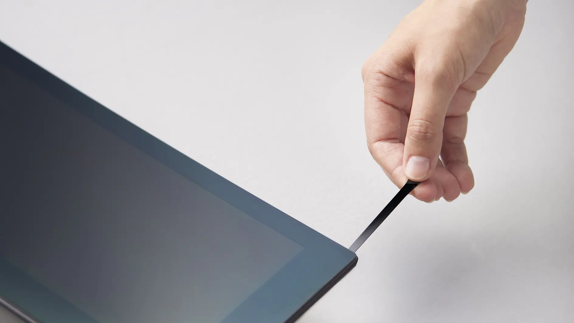 hand pulling black tesa strip from edge of laptop screen in a bright indoor setting