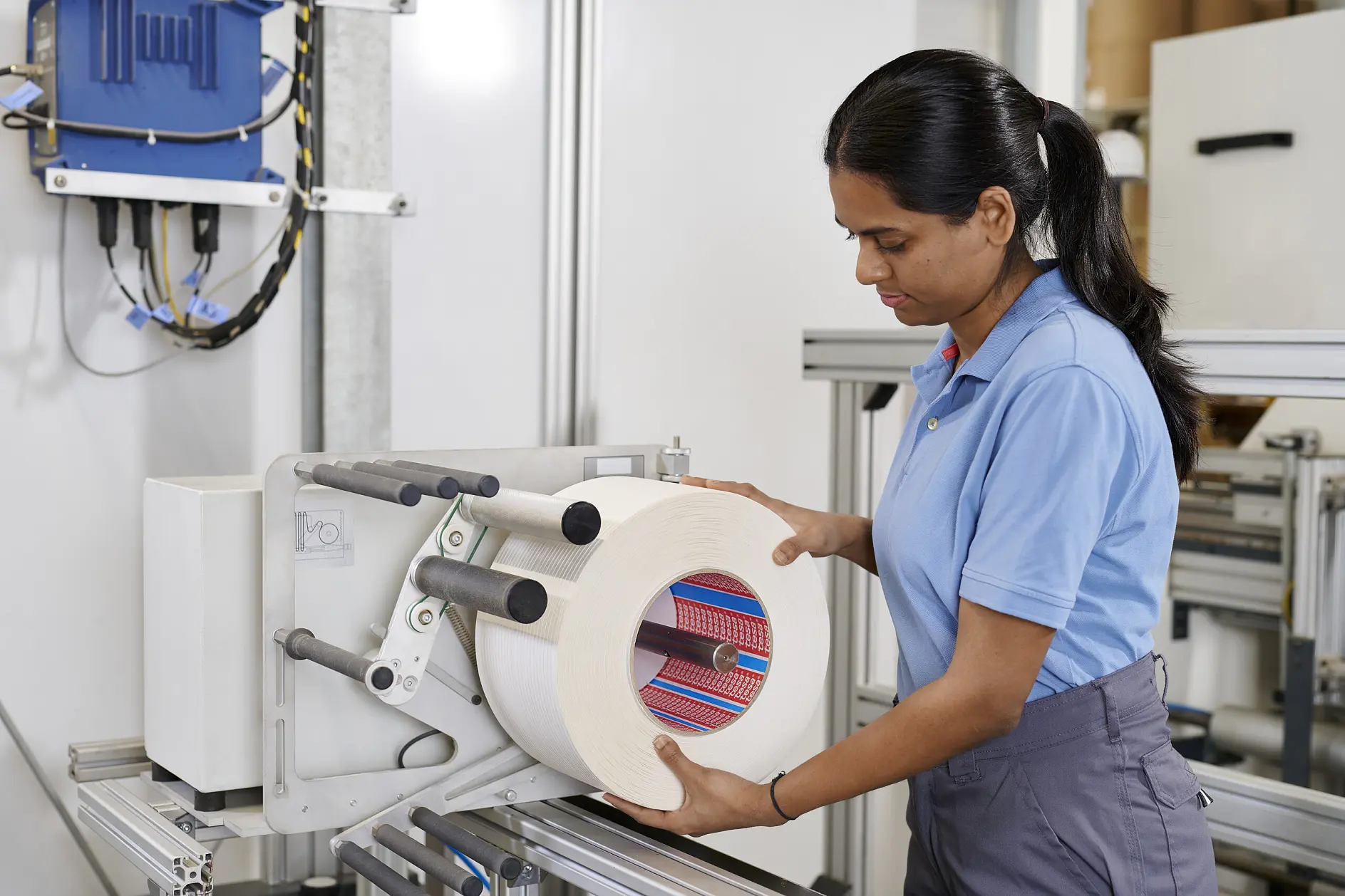 woman in blue tesa shirt operating a machine with a large roll of material in an industrial indoor setting