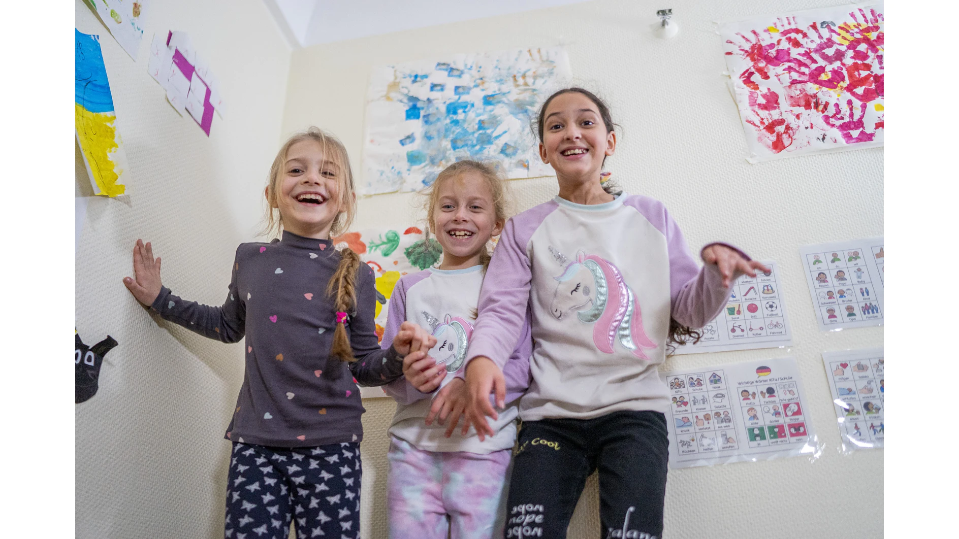 （从左到右）Larissa*，7岁，Svitlana*，7岁，以及Daniela*，11岁，在德国法兰克福为乌克兰难民设立的临时避难所内的儿童友好空间里对着镜头微笑。