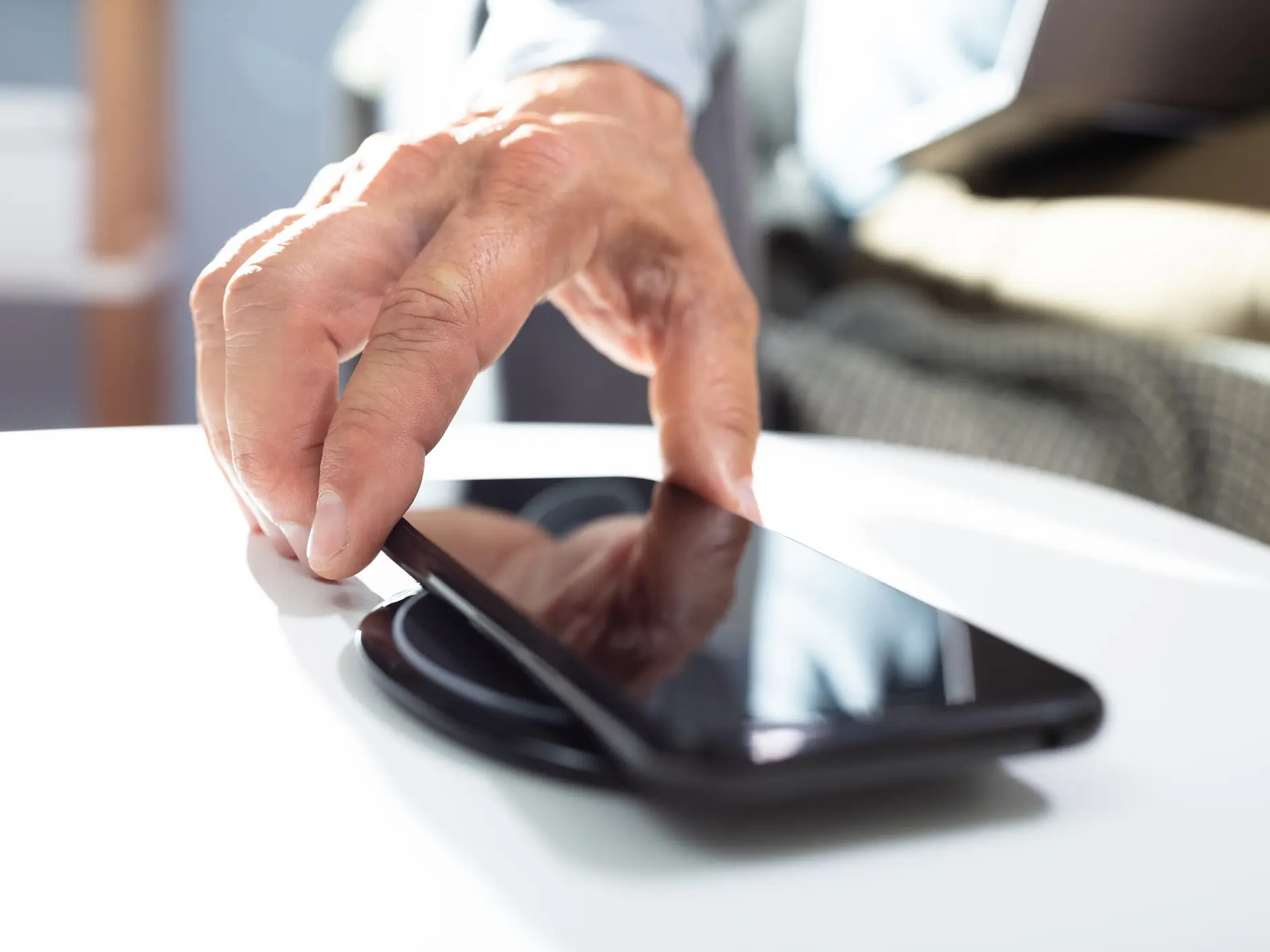 hand placing a black smartphone on a white table in a bright indoor setting with blurred background tesa