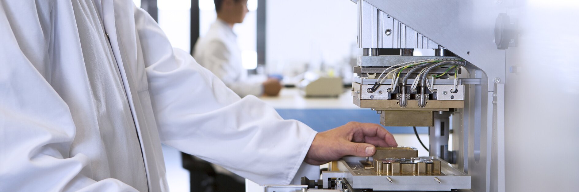 穿着实验室外套的科学家在明亮的实验室环境中操控自动测试设备，背景中有同事