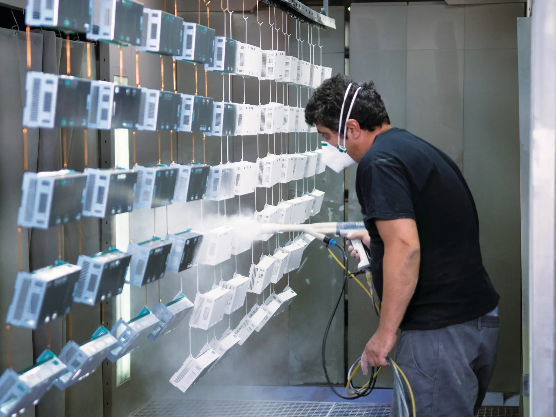 man in black shirt inspecting rows of hanging electronic devices in an indoor industrial testing facility (This text has been generated by AI)
