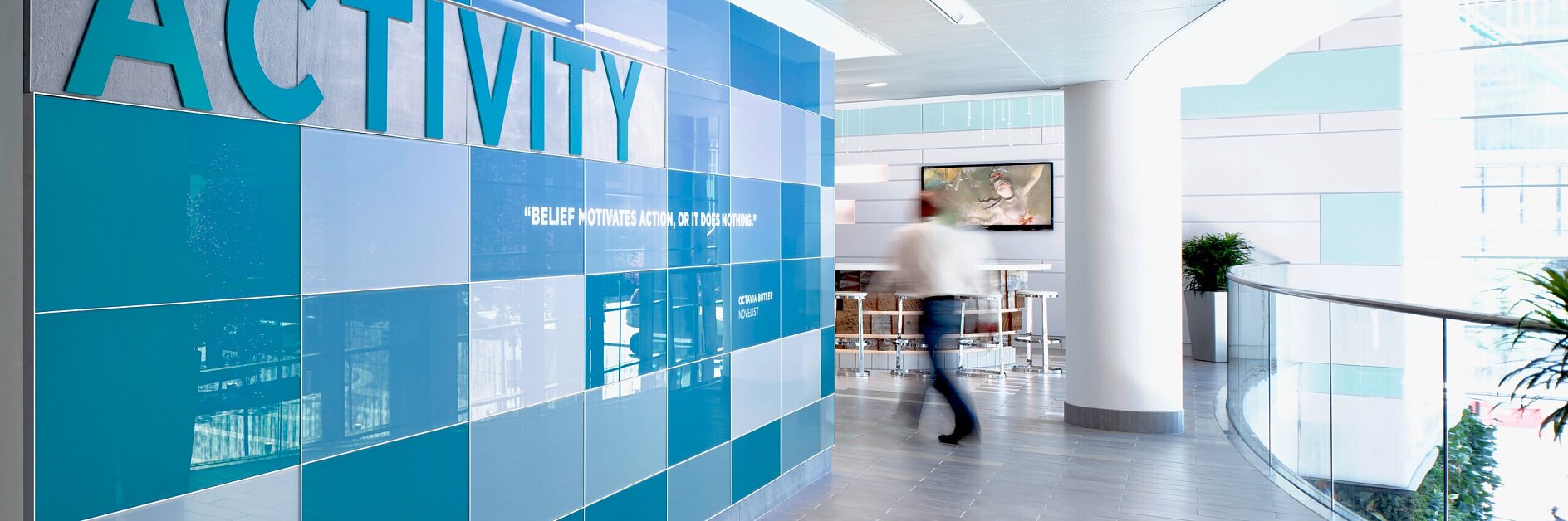 现代室内走廊，大型橙色和米色瓷砖墙上以粗体字显示“activity”，背景有人走过