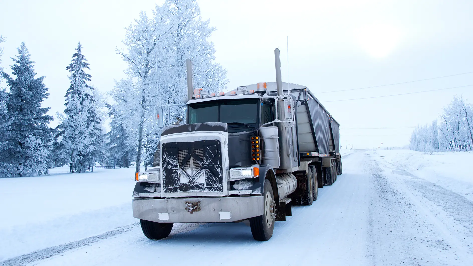 半挂卡车停在冰雪覆盖的乡村道路上，冬日雾气弥漫，背景中白色景色和树木被雪覆盖。